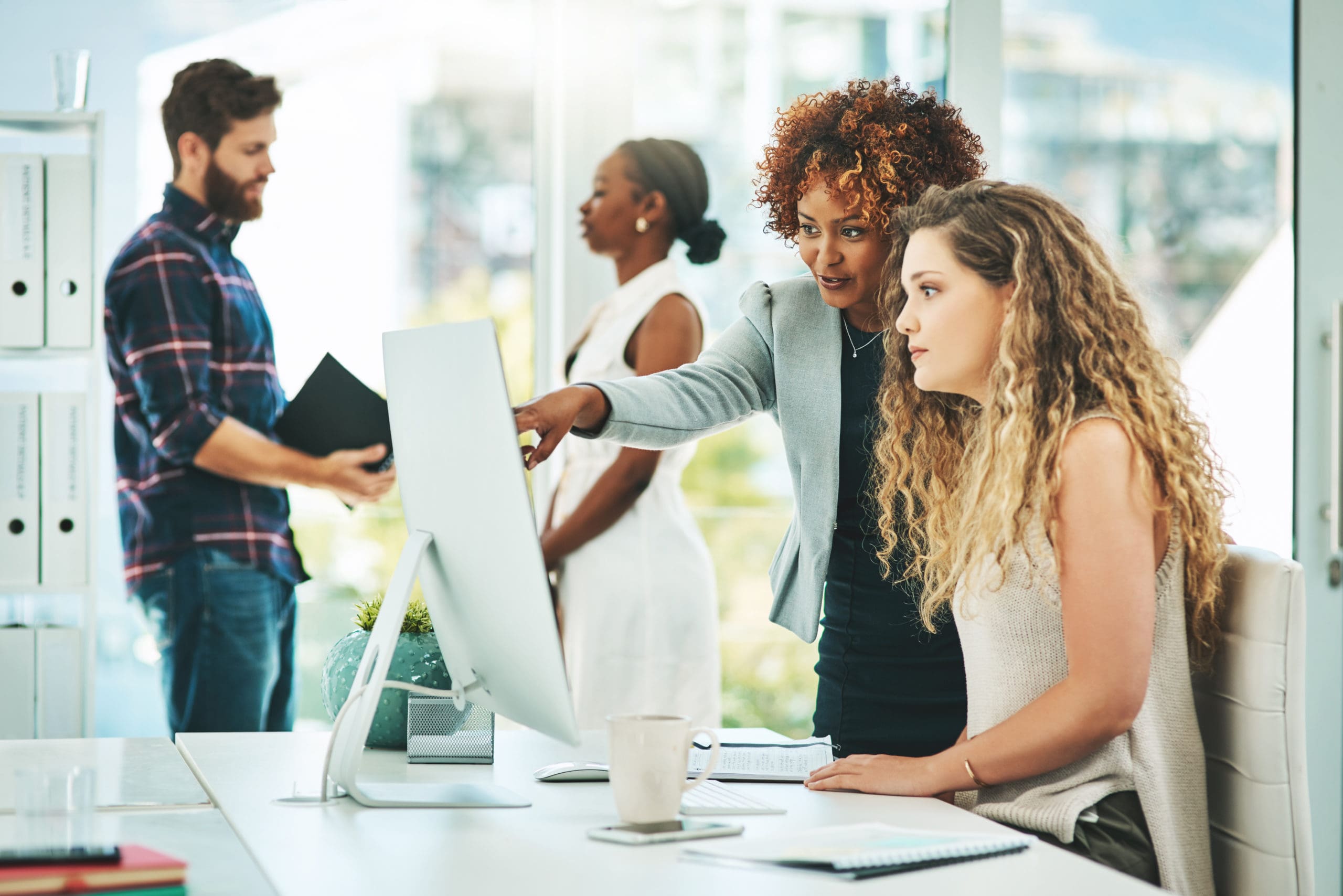 Shot of two businesswomen working together on a computer in an office with their colleagues in the background