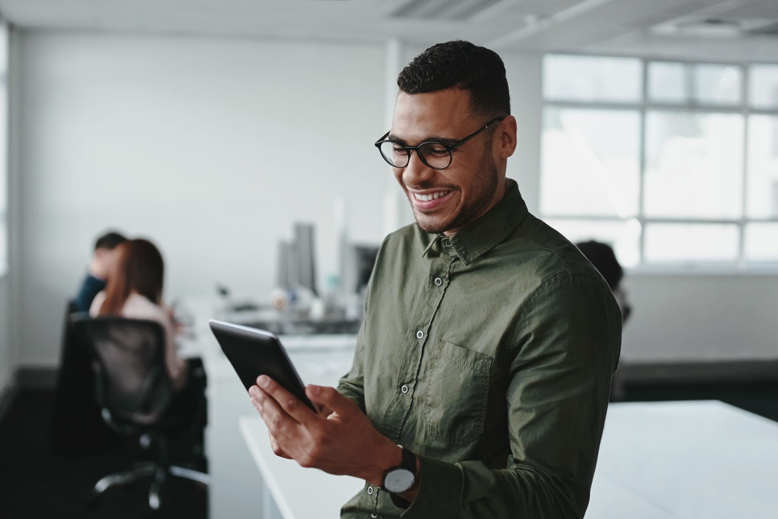 Smiling young businessman touching smartphone and checking online information in the modern office