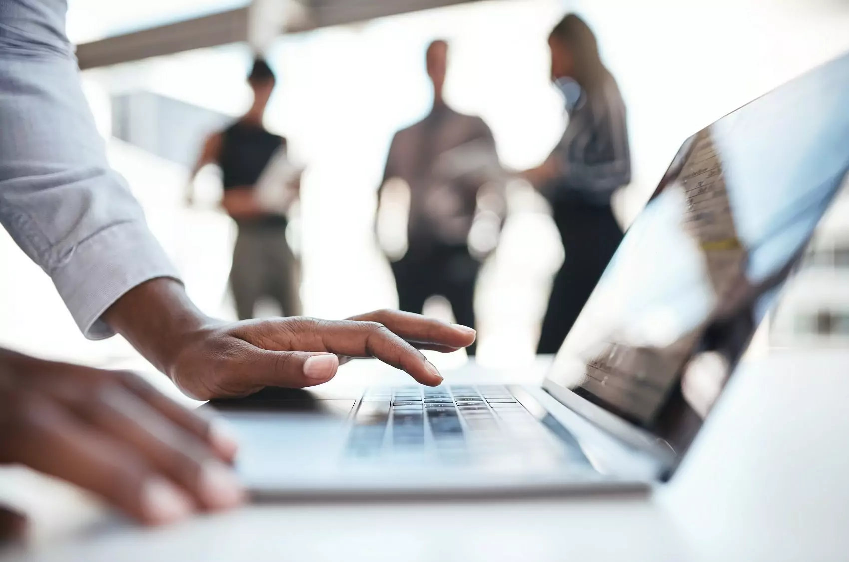 Cropped shot of an business person using a laptop while their colleagues stand in the background