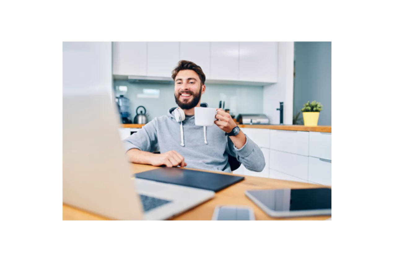 Young man holding a cup of coffee smiling while seated at his home office desk